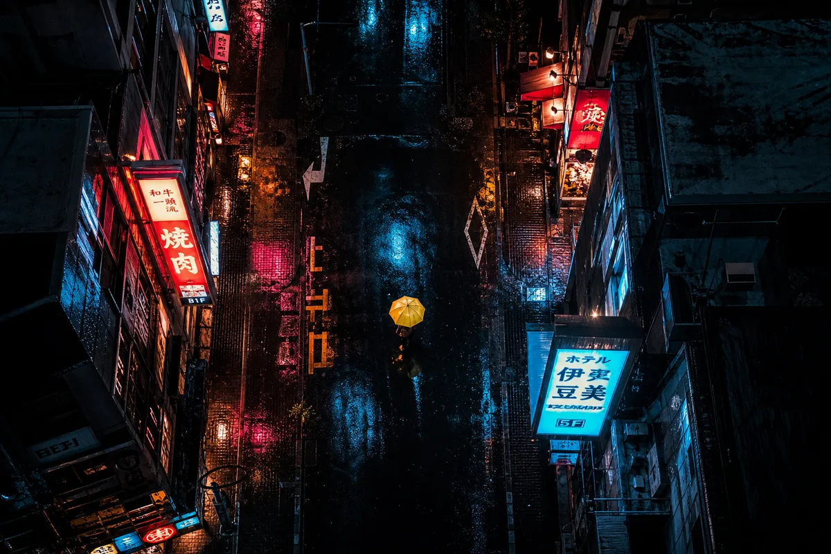 Night street, aerial — Top-down aerial view of a rain-soaked city street at night, neon signs reflecting on wet asphalt, a single yellow umbrella, cinematic, moody